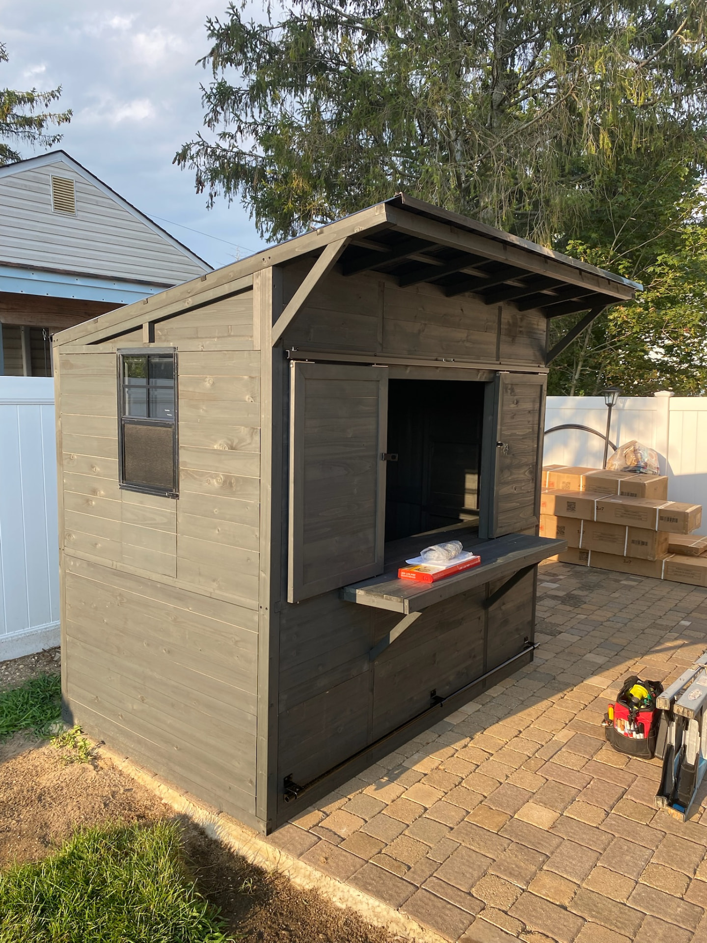 Completed gray outdoor storage shed with window and serving shelf